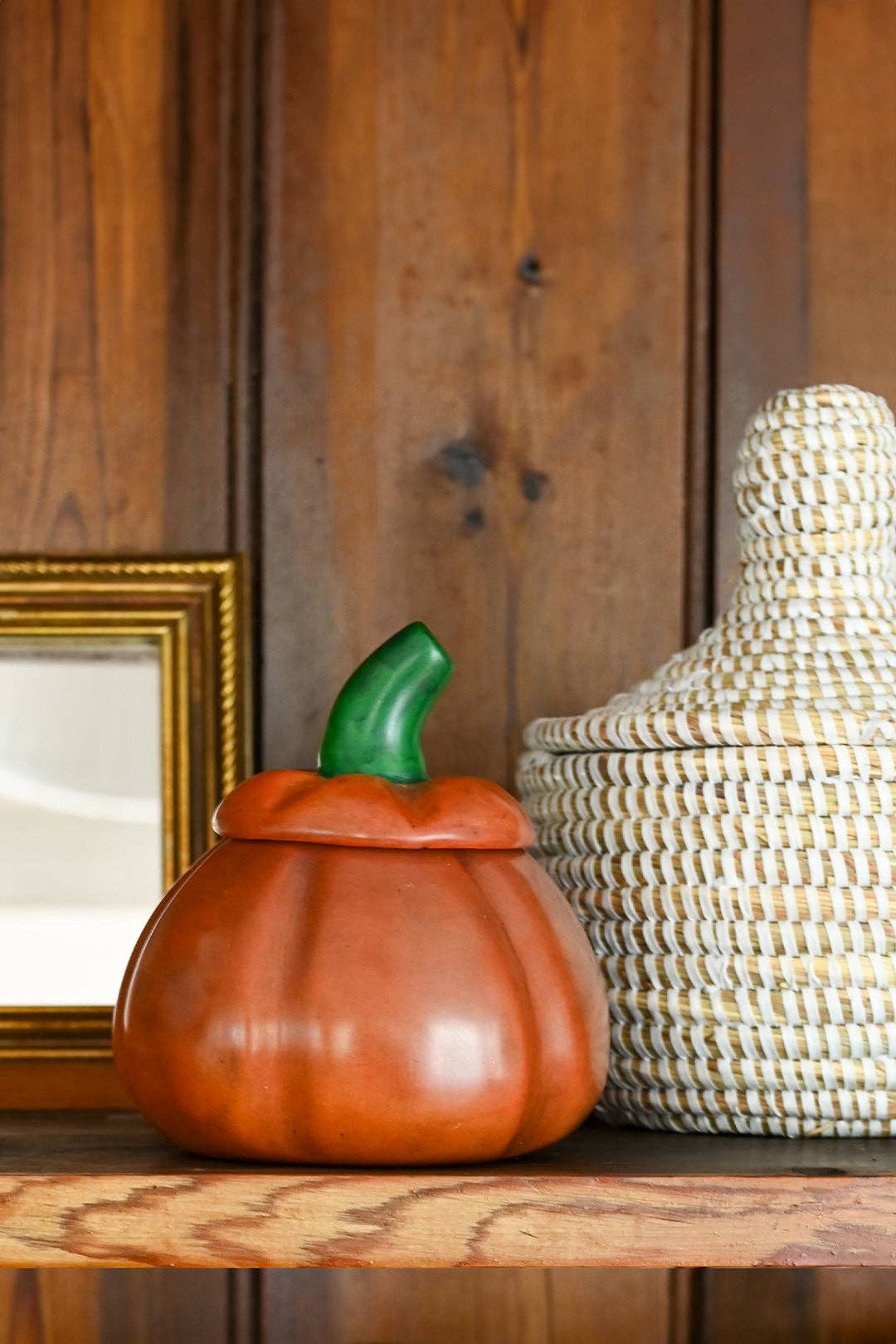 Decorative pumpkin-shaped container on a wooden surface with a woven basket in the background.