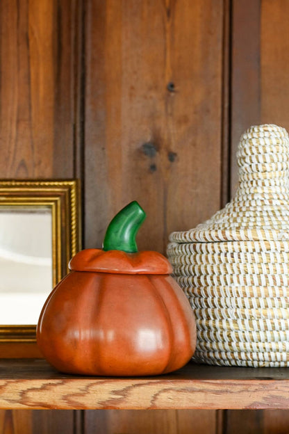 Decorative pumpkin-shaped container on a wooden surface with a woven basket in the background.