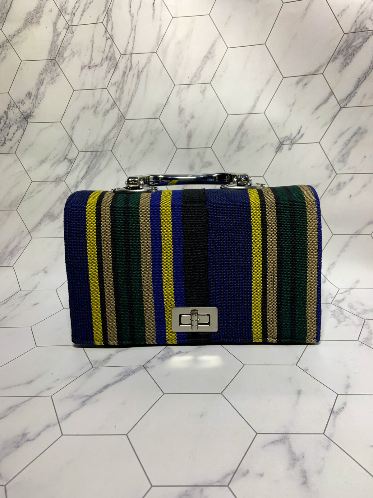 Striped handbag with blue, green, and yellow pattern on a marble floor.